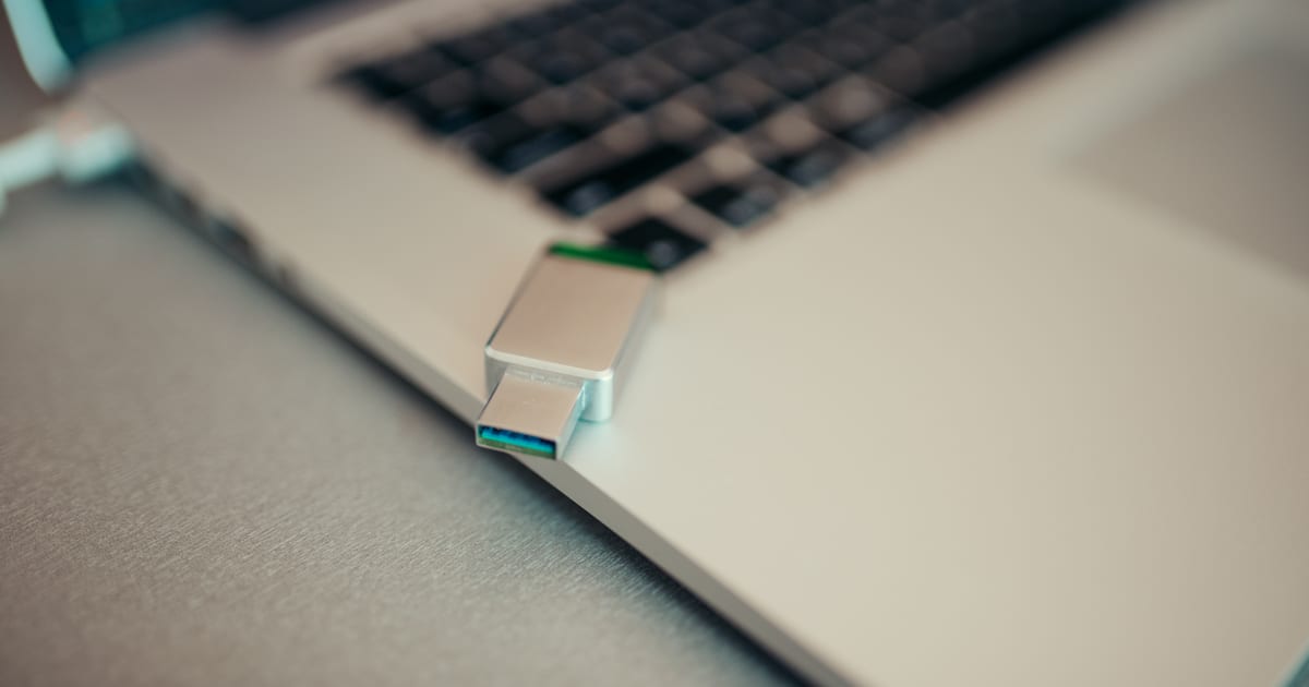 Pendrive com mídia de instalação conectado à lateral de um notebook sobre mesa clara