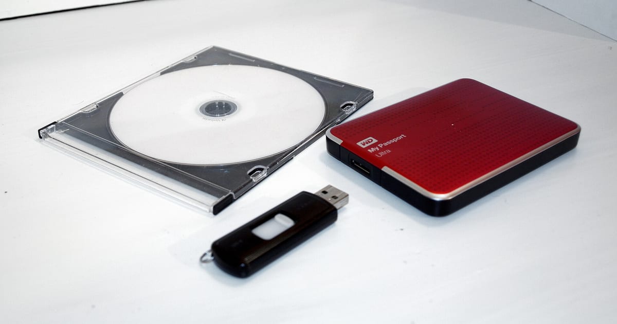 DVD, pendrive e HD externo lado a lado sobre uma superfície clara