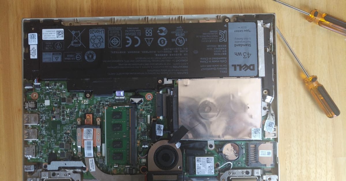 Notebook aberto na bancada com a tampa inferior removida, placa, bateria e chaves de precisão ao lado
